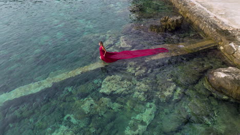 woman in red dress with long trail swims in the adriatic sea in croatia