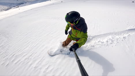 man wearing sport suit and protective glasses rides down the hill on his snowboard. snowboarder taking selfie video.