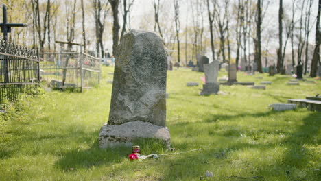 grabstein mit einer roten rose und einer grabkerze auf dem gras auf einem friedhof an einem sonnigen tag