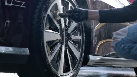 vista recortada de unas manos masculinas en guantes de protección negros, limpiando las llantas de la rueda de aleación del coche con un pincel