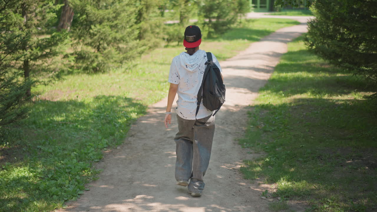 Journeying with resolve, Adventurer advances confidently through bright woodland walkway with purpose, Explorer moves purposefully down sunlit pathway amidst shining trees in forest