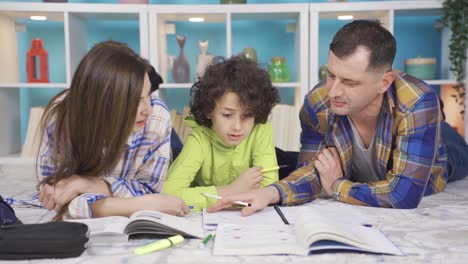 Glückliche-Familieneltern,-Die-Zu-Hause-Auf-Dem-Warmen-Boden-Liegen-Und-Ihrem-Süßen-Jungen-Beim-Unterricht-Helfen.