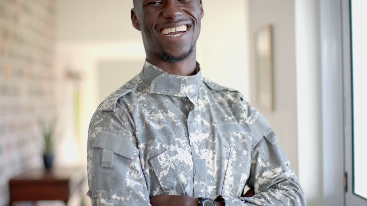 feliz soldado afroamericano de pie y sonriendo en la sala de estar soleada, cámara lenta