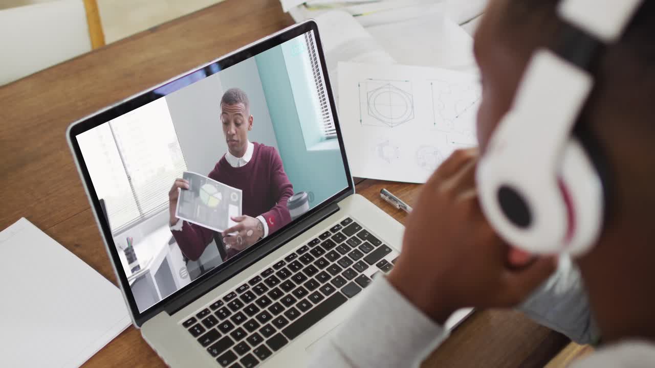 estudiante universitario afroamericano que sostiene notas mientras hace una videollamada en una computadora portátil en casa