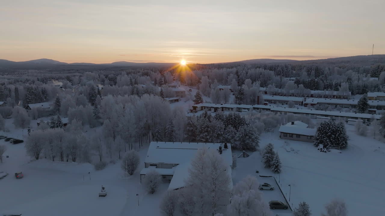 Aerial view of arctic sunrise above houses and frosty trees in a town of Lapland