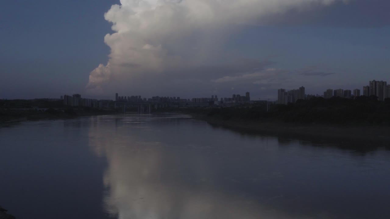 una escena tranquila del río al anochecer con las luces de la ciudad reflejadas en el agua mientras una gran nube se eleva sobre la cabeza, creando una atmósfera tranquila a medida que el día se convierte en noche