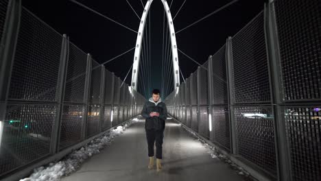 Wide-shot-of-a-man-texting-and-walking-on-a-bridge-at-night-in-the-city