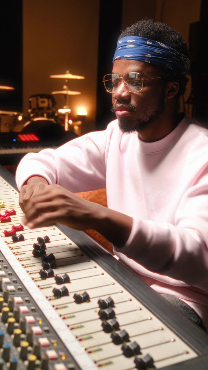 Focused Black Audio Engineer Adjusting Faders on Mixing Desk in Recording Studio