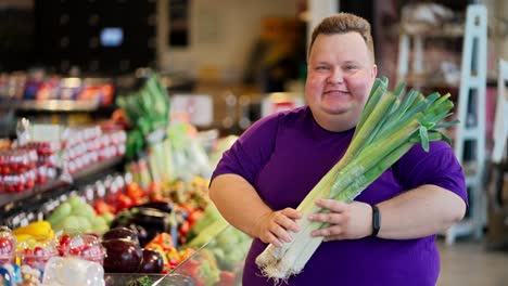 Portrait-of-a-Happy-and-joyful-overweight-man-in-a-purple-T-shirt-who-holds-a-bunch-of-shallots-in-his-hands,-sniffs-them-and-smiles-in-a-large-supermarket