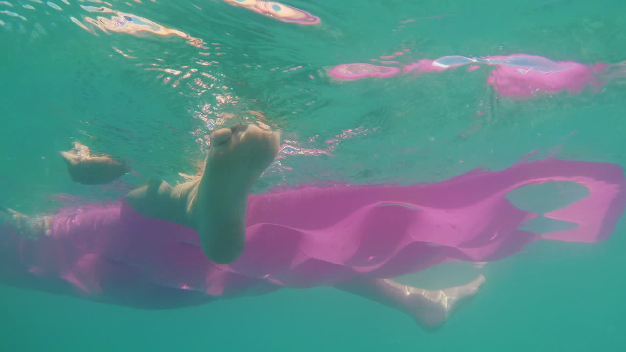 그의 다리가 매달려있는 바다의 파도에 흔들리는 팽창식 매트리스를 수중 촬영