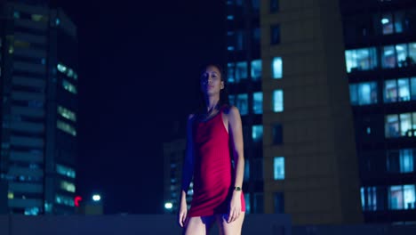 On a rooftop with the Caribbean city lights of Port of Spain, Trinidad behind her, a Hispanic girl stands.