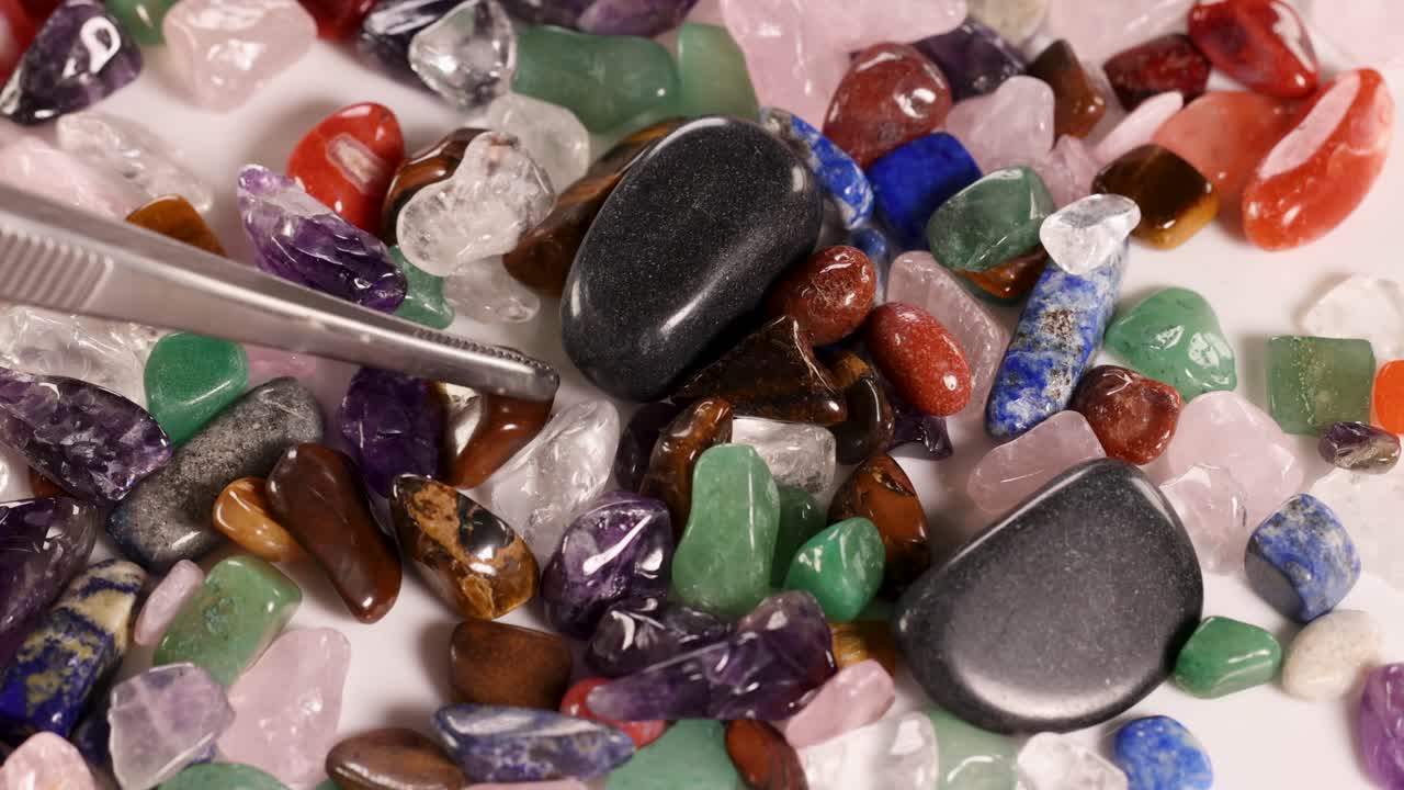 A close-up view of various chakra stones being sorted with tweezers under bright lighting