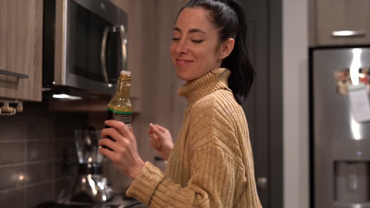 Young funny woman joking around while she dances and cooks dinner in her modern kitchen - concept: healthy lifestyle, radiant, date night, silly - medium shot