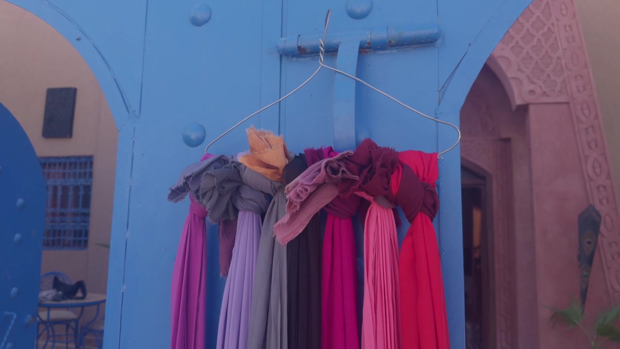 Multiple colorful draped fabric scarves hanging on a single wire hanger against a bright blue wooden door