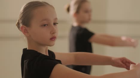 a group of young ballet students in black dancewear practicing positions in a spacious ballet studio with wooden flooring and wall-mounted barres. focused expressions and synchronized movements.