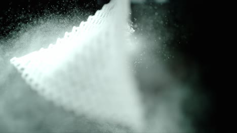 a piece of woven mesh fabric that is hanging is shaken which releases a cloud of white powder