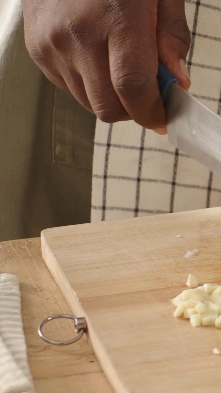 Video verticale: Una mano entra con un coltello blu, un cuoco in grembiule trita l'aglio in cucina.