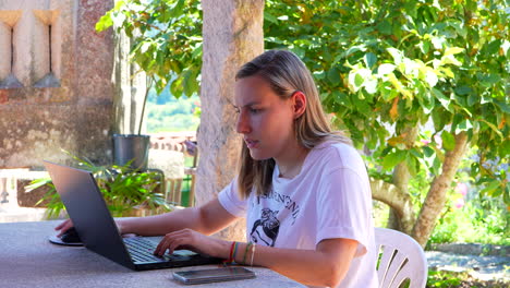 atractiva mujer caucásica escribiendo en la computadora portátil remotamente en el jardín
