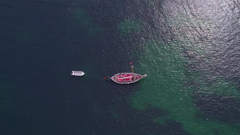 Top-down-shot-of-anchored-sailing-boat-on-a-calm-ocean-near-Ponta-da-Piedade-Portugal,-aerial