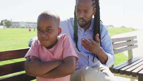 Video-of-african-american-father-sitting-on-bench-and-talking-with-angry-son