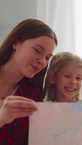 joyful teenage girl with admired sister look at painting in ebru style in apartment closeup slow motion. traditional marbling design technique for family