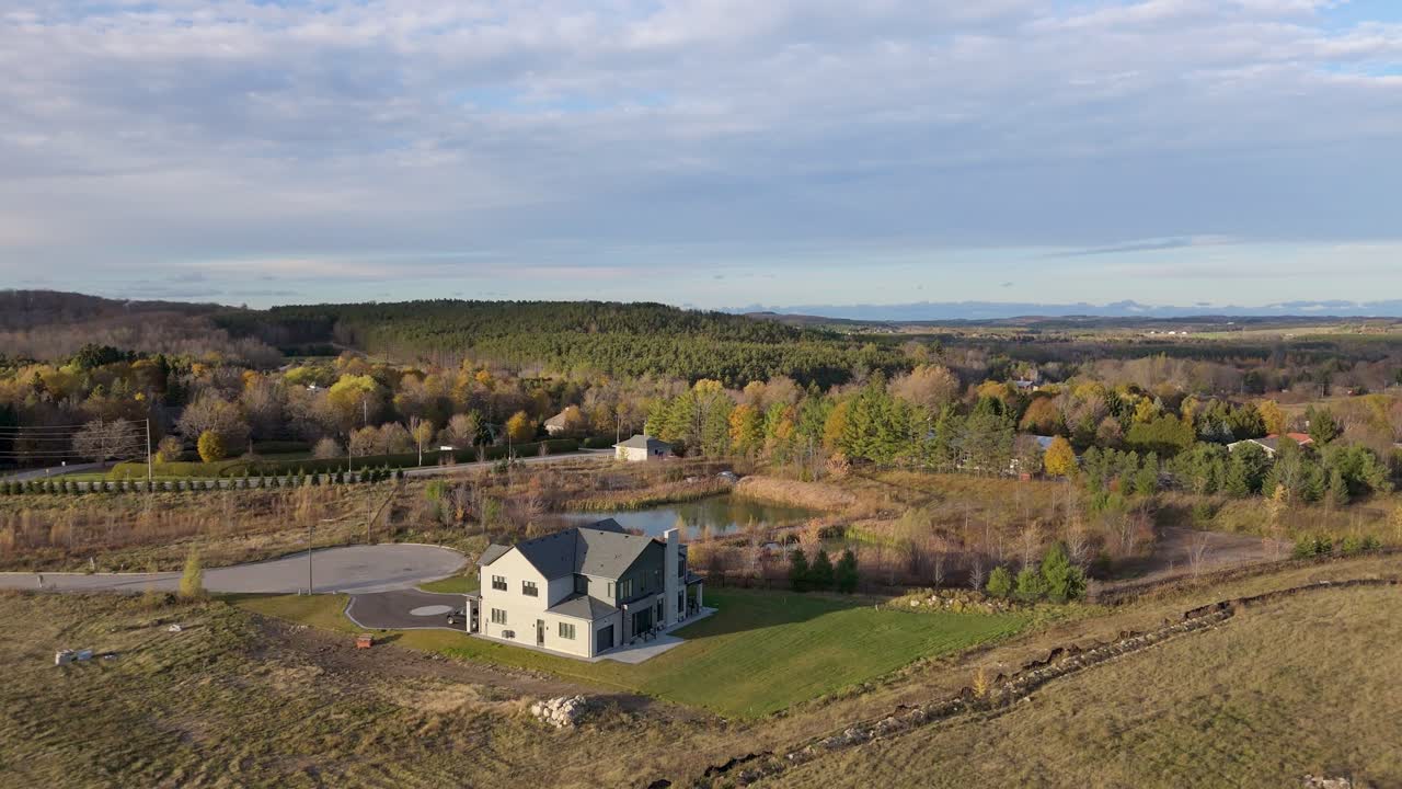 Drone shot of a newly built home surrounded by rolling hills, ponds, and autumn forest in Caledon, Ontario, capturing late-fall colours across the countryside landscape