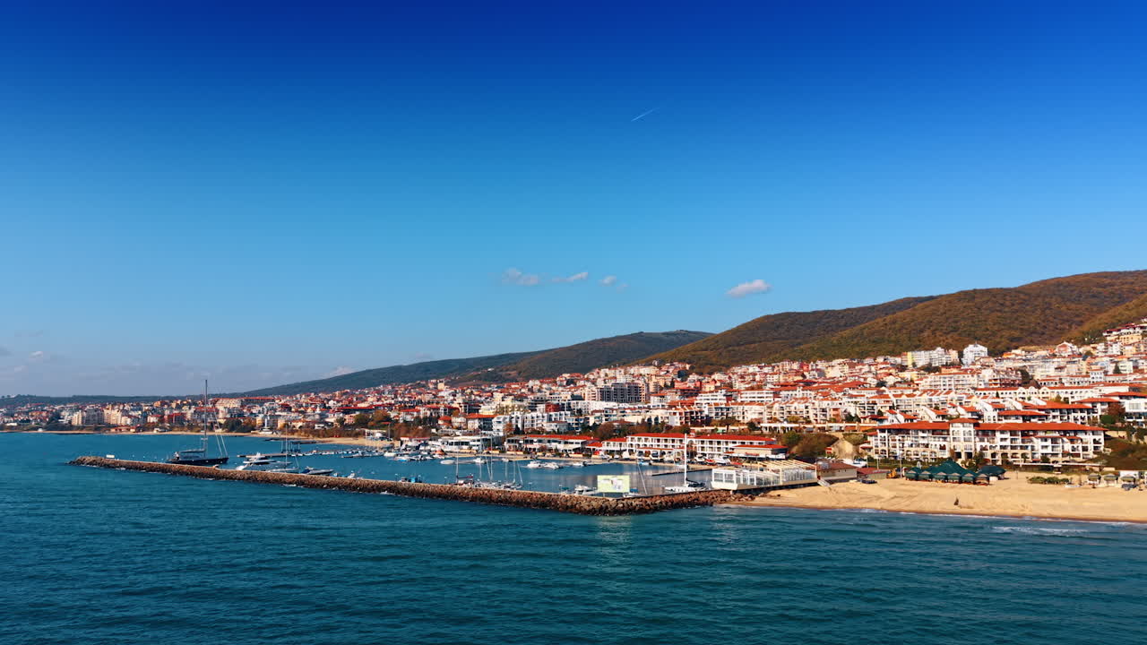 Vista costiera di una località balneare in riva al mare sotto un cielo azzurro. Persone si godono una giornata di sole sulla spiaggia vicino all'acqua, con edifici sullo sfondo