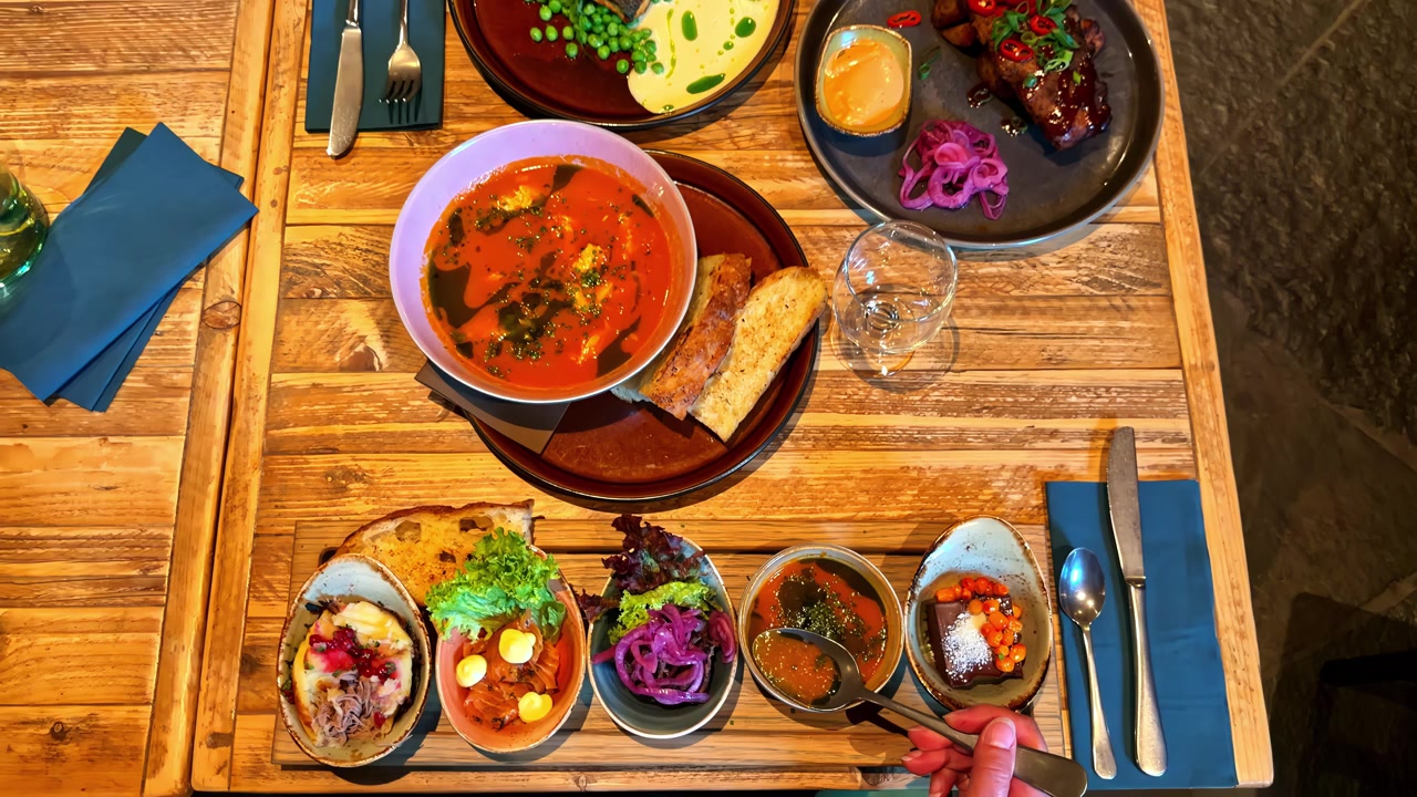 Hand sampling assorted Nordic dishes and soup at rustic wooden restaurant table