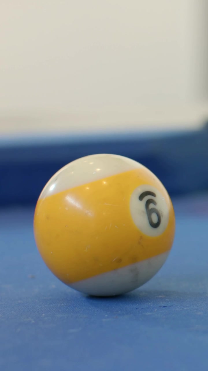 Vertical video: Tilting yellow-white ball #6 rolling after tap on blue pool table, red ball chasing
