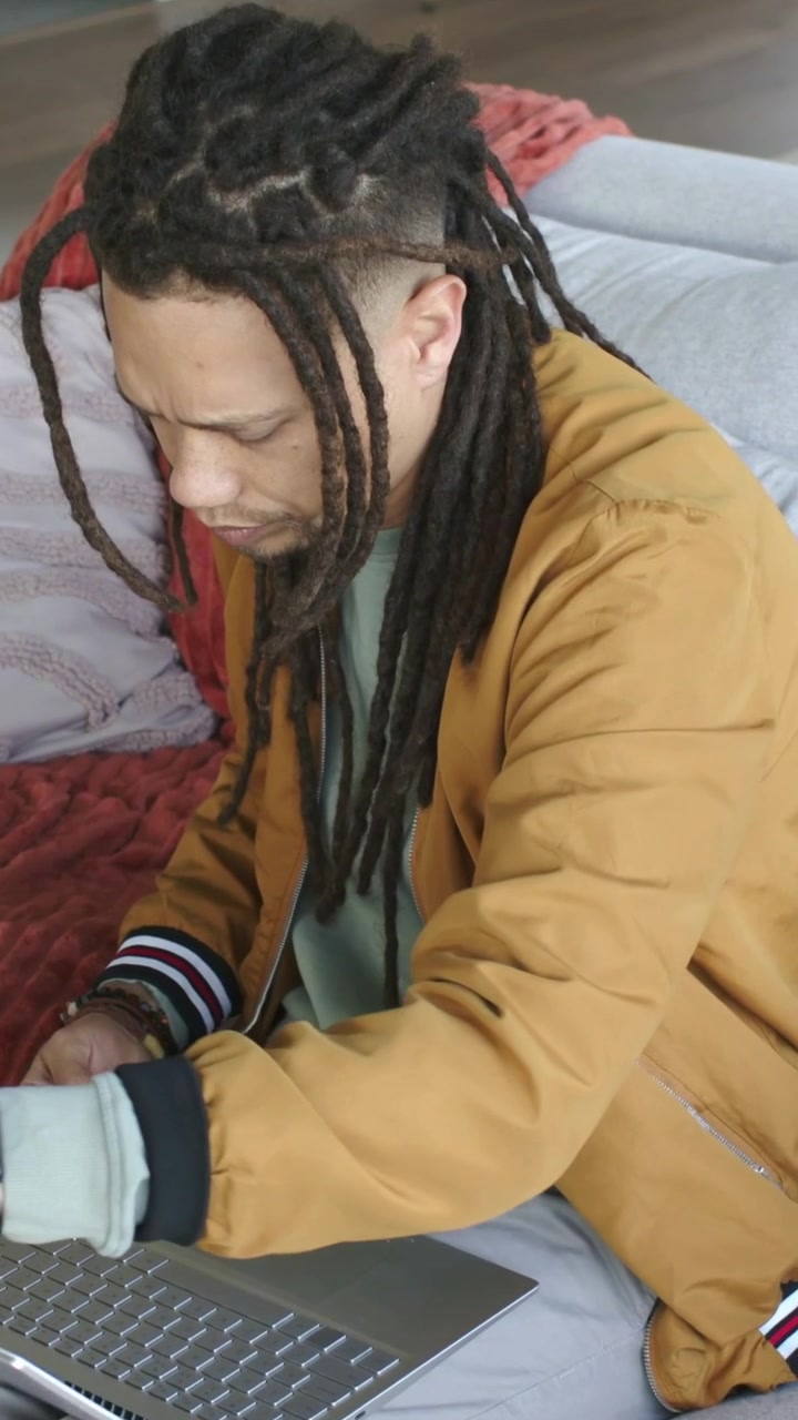 Vídeo vertical: Vendo laptop, homem com jaqueta marrom digitando e ajustando a tela para trabalhar no sofá