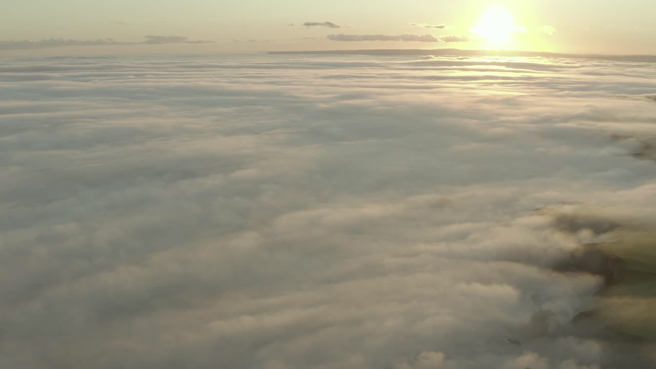 Aerial tilt up from foggy Irish coastline to sunset over sea of cloud