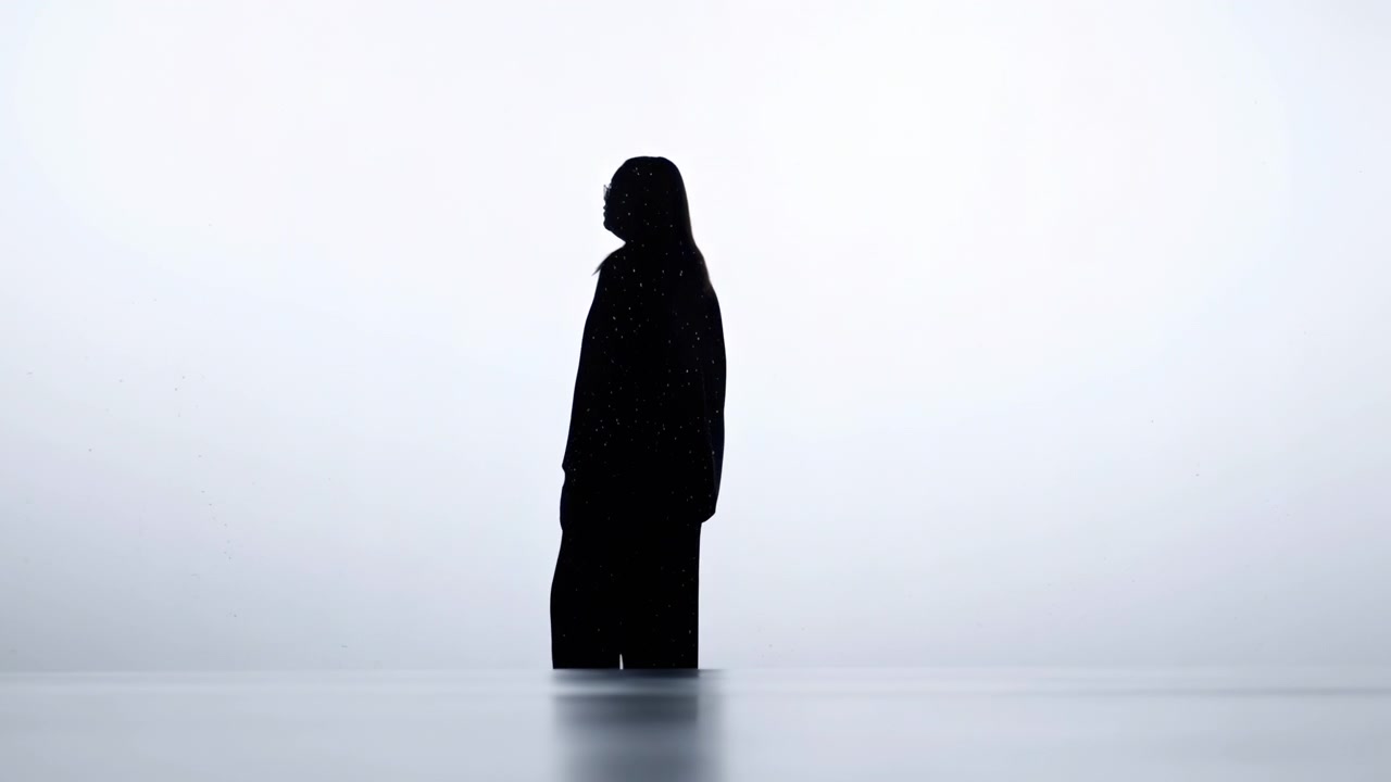 A serene, minimalistic silhouette of a person standing in a neutral indoor setting with a light background, captured from a side view perspective. The scene features a clean, black andwhite.