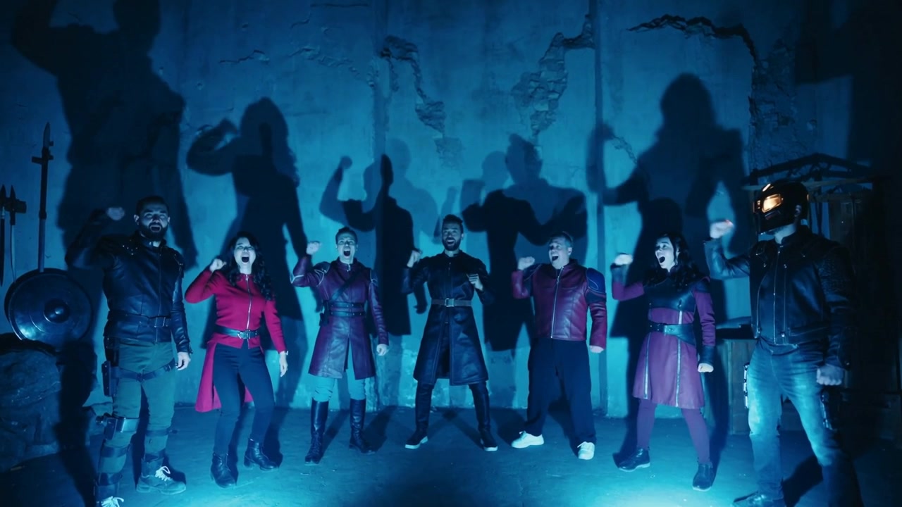 Chanting after cue, ensemble of eight raising fists in warehouse for show, blue lights, helmet