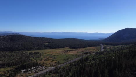 Aerial-shot-of-cars-driving-through-a-stunning-tree-dotted-valley-towards-Lake-Tahoe-in-Nevada