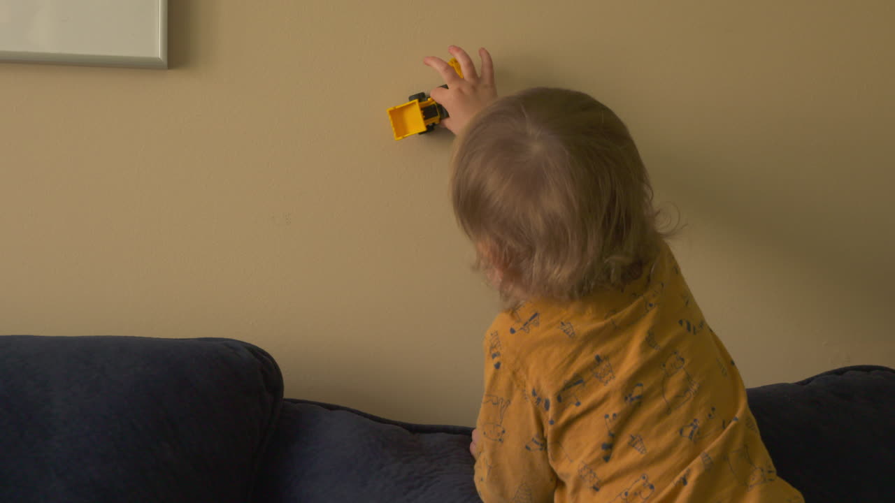 Toddler boy pushing a toy truck around a wall