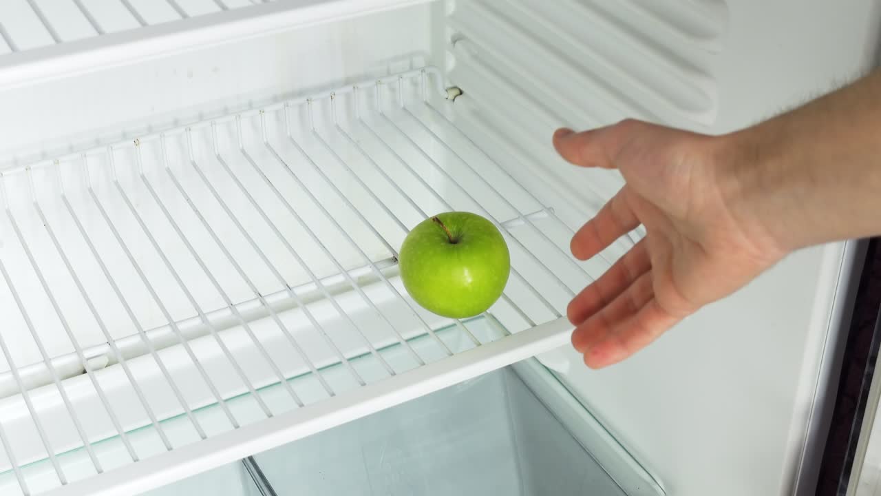 la mano del hombre abre un refrigerador vacío con la palabra crisis y toma una sola manzana verde. video en bruto conceptual 4k idea de crisis económica, escasez de alimentos, pobreza.