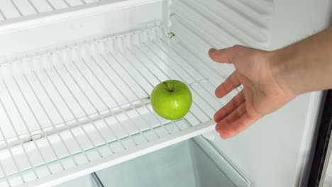 the man's hand opens an empty refrigerator with the word crisis on it and takes one single green apple. conceptual 4k raw video. idea of ​​economic crisis, food shortage, poverty.