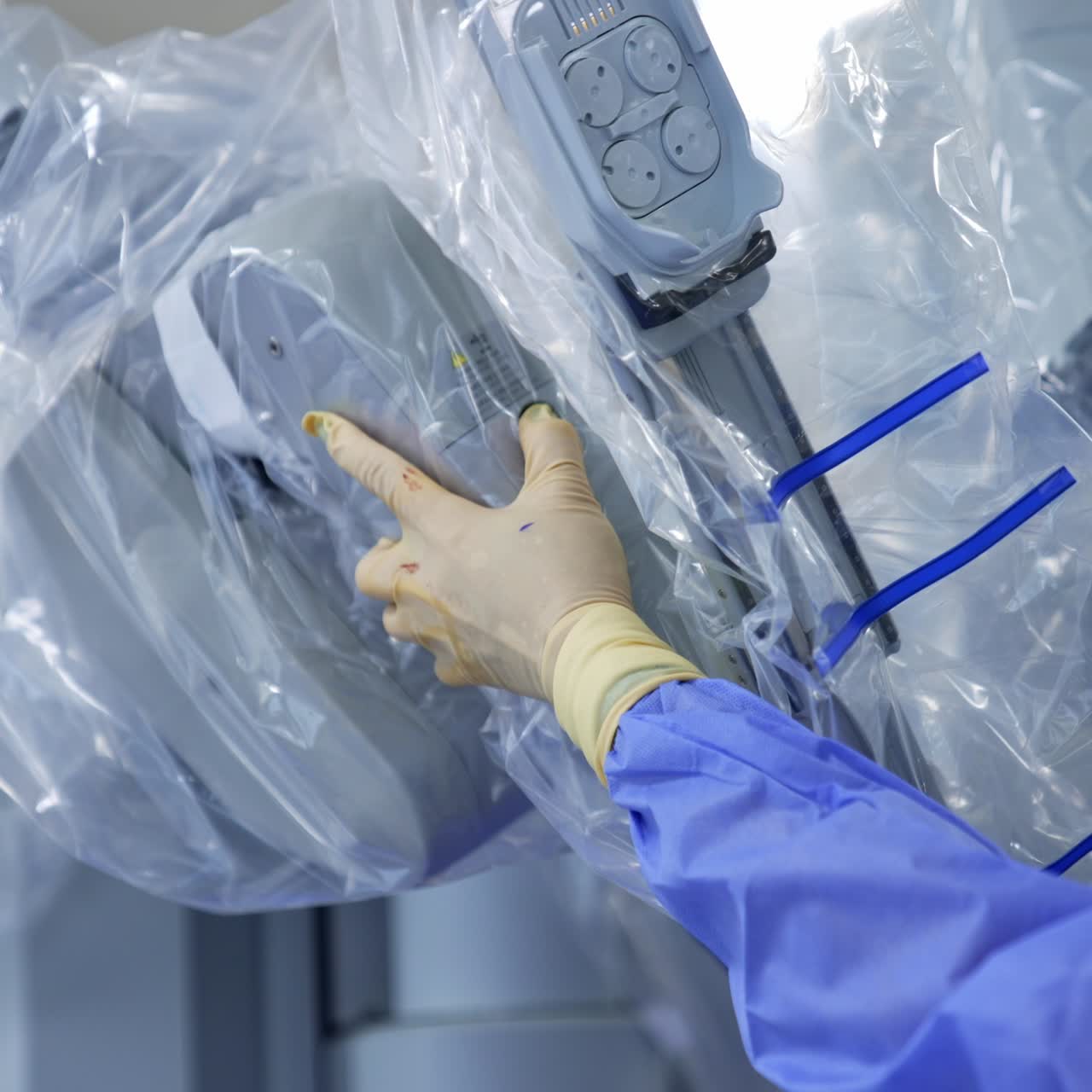 Hand in latex gloves and blue uniform pulling the robotic arm covered with plastic. Medic preparing advanced equipment for usage at surgery