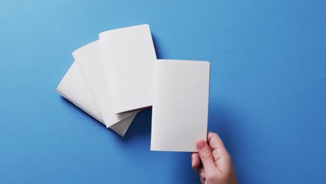 Hand-holding-piece-of-paper-over-pieces-of-paper-with-copy-space-on-blue-background-in-slow-motion