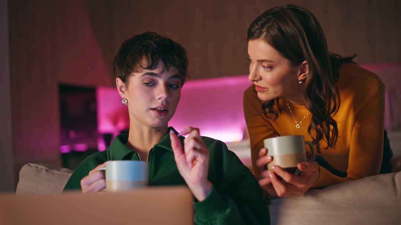 Donna che condivide un caffè con un'amica che naviga al laptop in un primo piano serale domestico