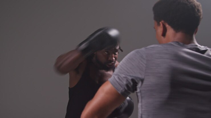 Scatto in studio di un pugile uomo che fa sparring e si allena con l'allenatore, indossando guanti da passata o guantoni, preparandosi per un incontro 2