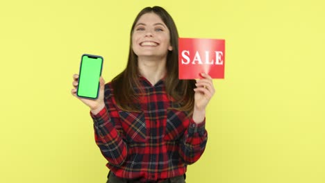 satisfied brunette woman holding green screen smartphone and red sale card
