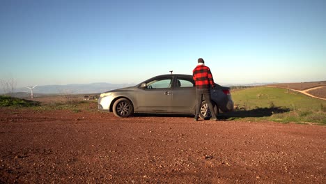 hombre caucásico barbudo saliendo de un coche gris de 4 puertas y agarrando una mochila, israel