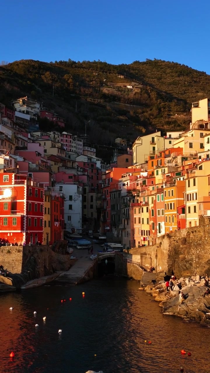 Mouvement lent de drone vers les maisons colorées de Riomaggiore et le littoral rocheux au coucher du soleil, Cinque Terre, Italie.