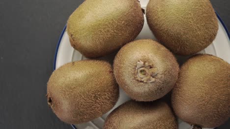 kiwi fruit. ripe kiwis in a white plate with a blue border rotate on a gray stone background.