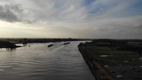 Ship-And-Cargo-Barge-Sailing-Across-The-Quiet-River-Of-Oude-Maas-With-Cars-Park-Offshore-Town-Of-Zwijndrecht-In-Netherlands