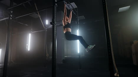 workout in sport club young slender woman is hanging on crossbar and lifting legs up