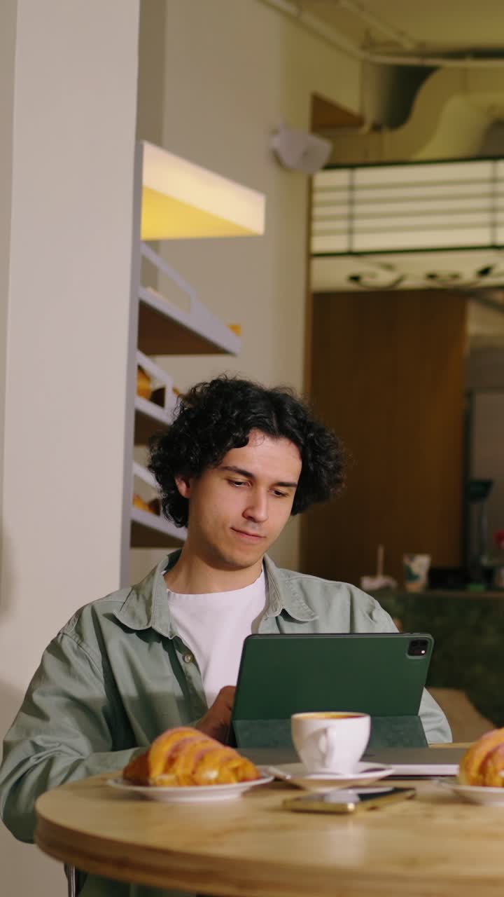 Giovane uomo che usa un tablet mentre gusta caffè e croissant al bar