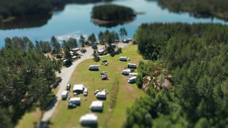 tens of motorhomes, minivans, and cars parked in kilefjorden camping are seen from the air on a sunny day