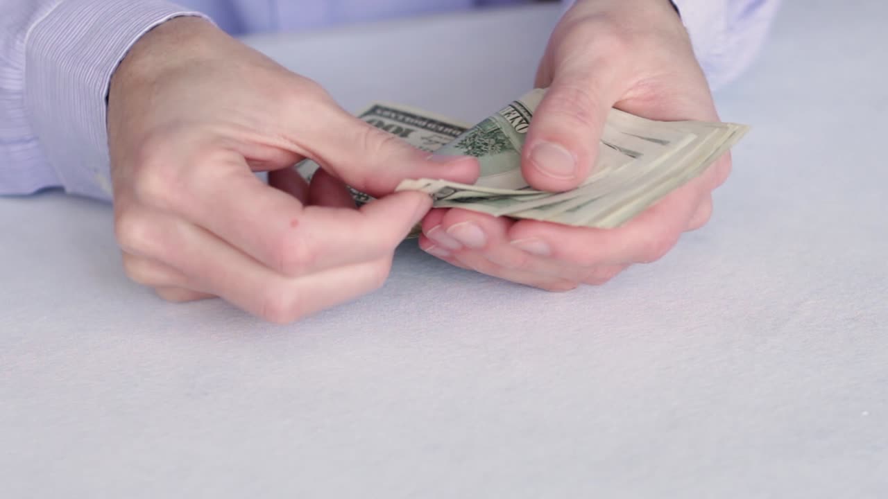 Mani che contano un mazzetto di banconote da 100 dollari USA.